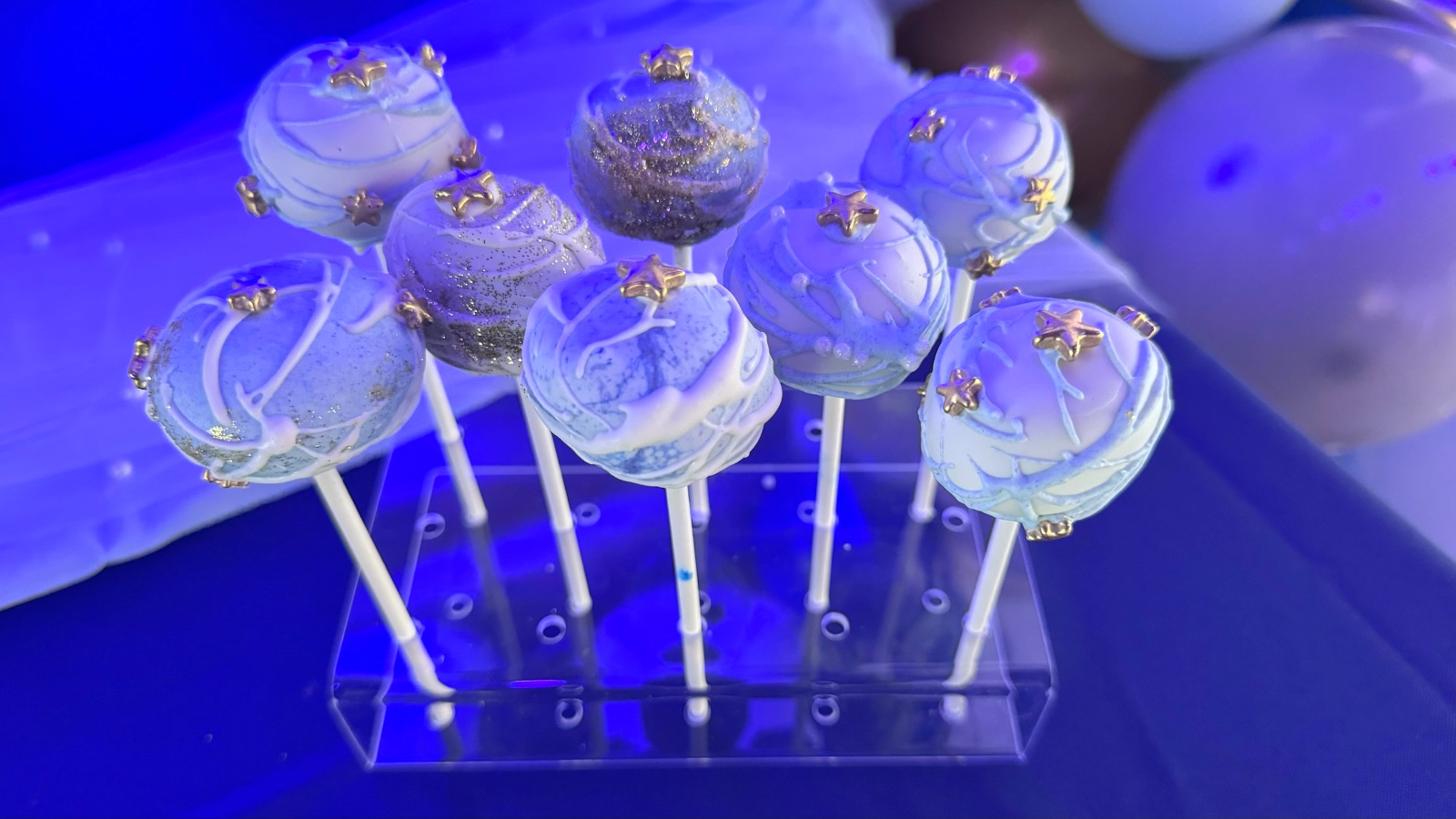 Cake pops en azul pálido y brillo plateado con estrellas doradas en una base acrílica