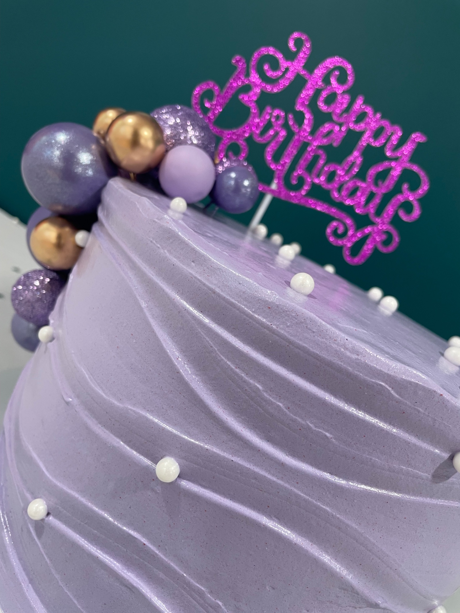 Pastel de cumpleaños lavanda con esferas doradas y moradas