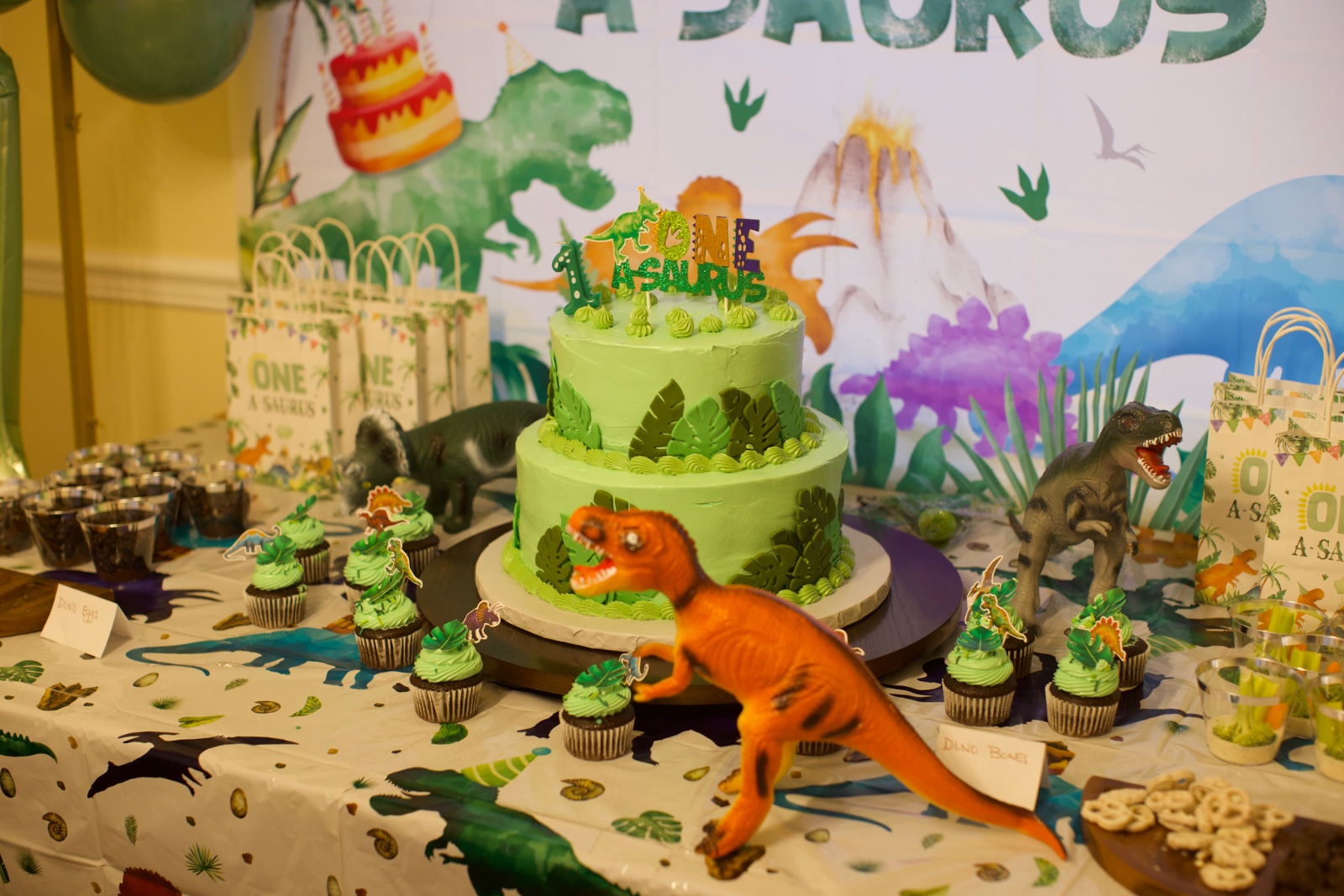 Mesa de postres de primer cumpleaños con pastel verde de dinosaurio y cupcakes