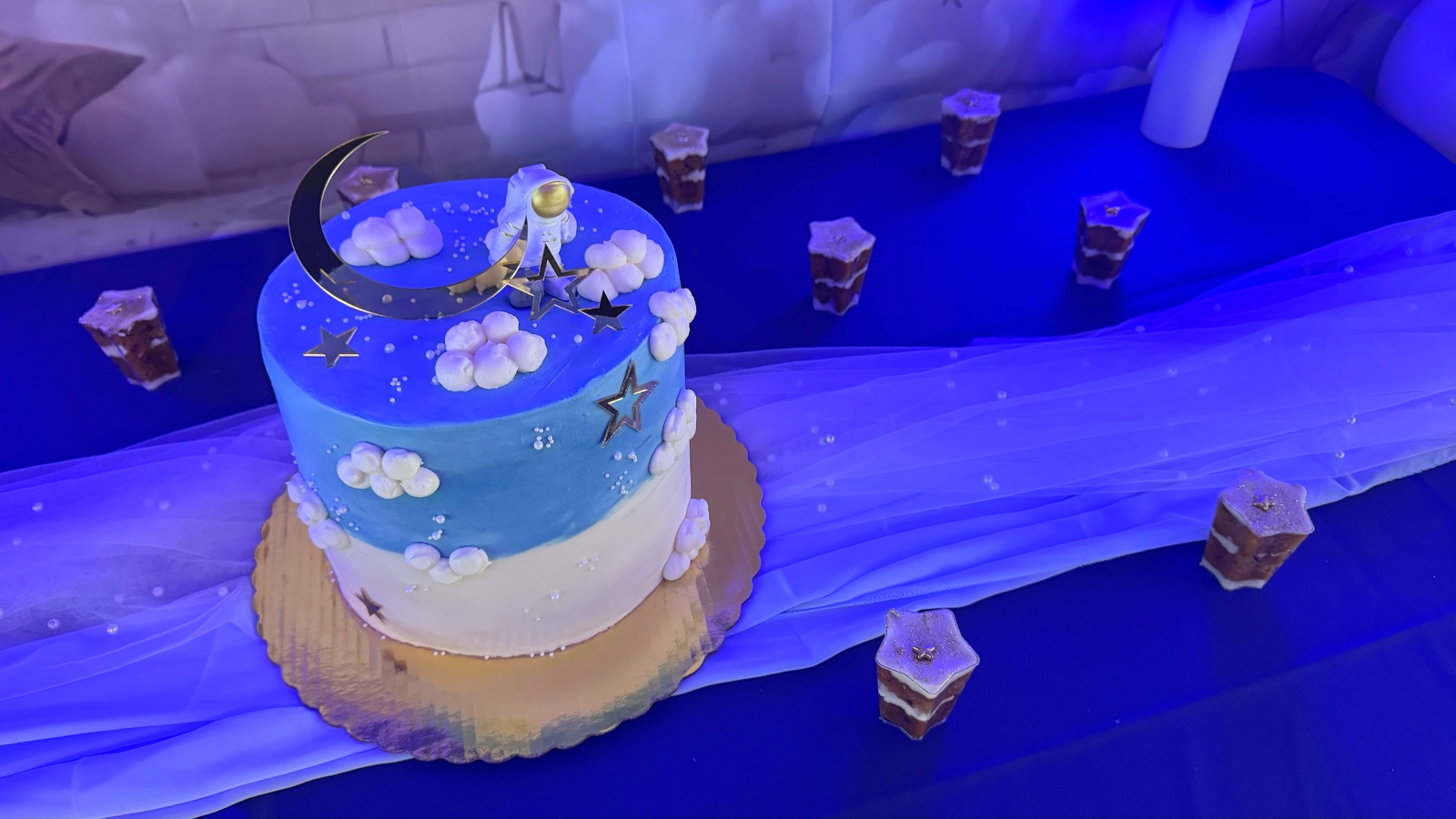 Pastel azul y blanco con nubes de crema, estrellas doradas y figura de astronauta con luna creciente